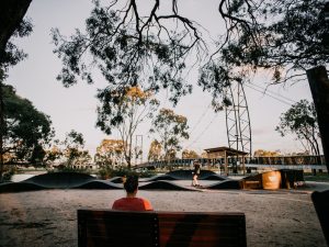 image of lady sitting on park bench watching someone on a bike on the pump track
